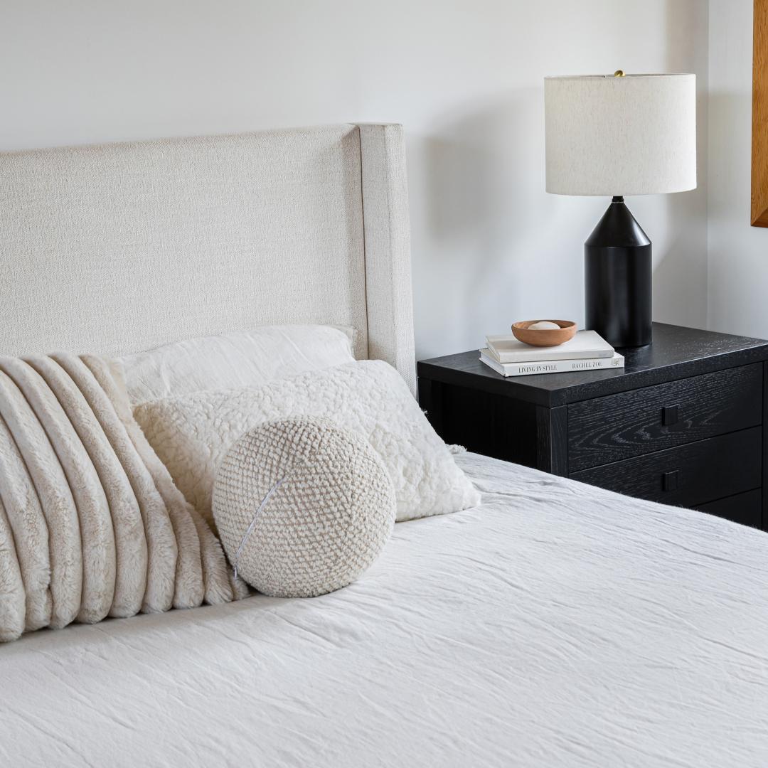Neatly made bed with decorative pillows and a lamp on a nightstand in a bedroom setting.