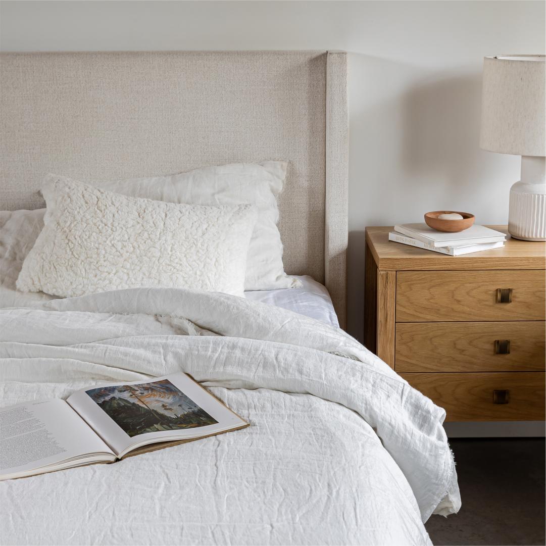 Bedroom with a bed featuring white bedding and pillows, a wooden nightstand with a lamp and books.