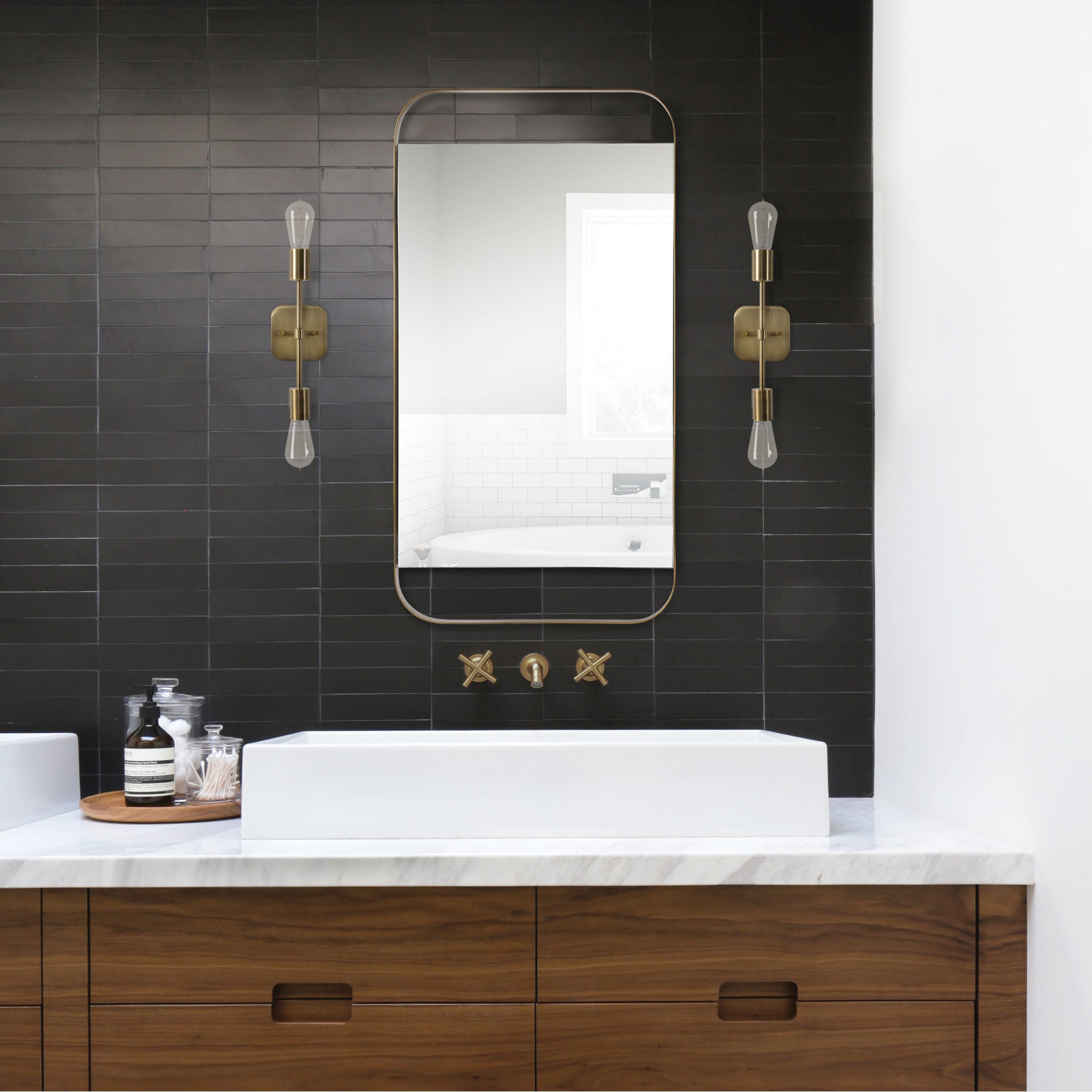 Zariyah mirror with a sleek gold frame, mounted above a modern sink in a stylish bathroom with black tiles.