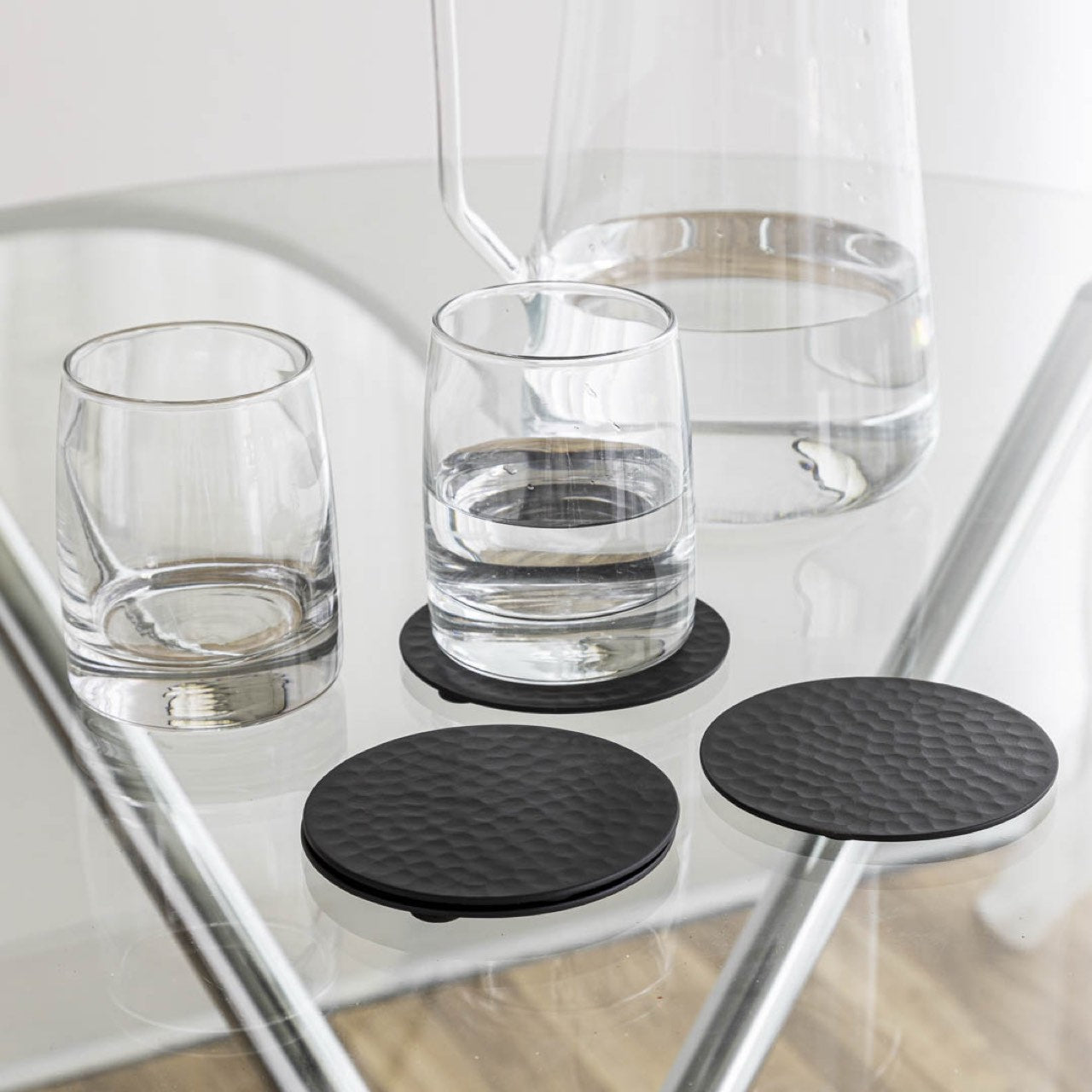 Black coasters on a glass table with glasses of water