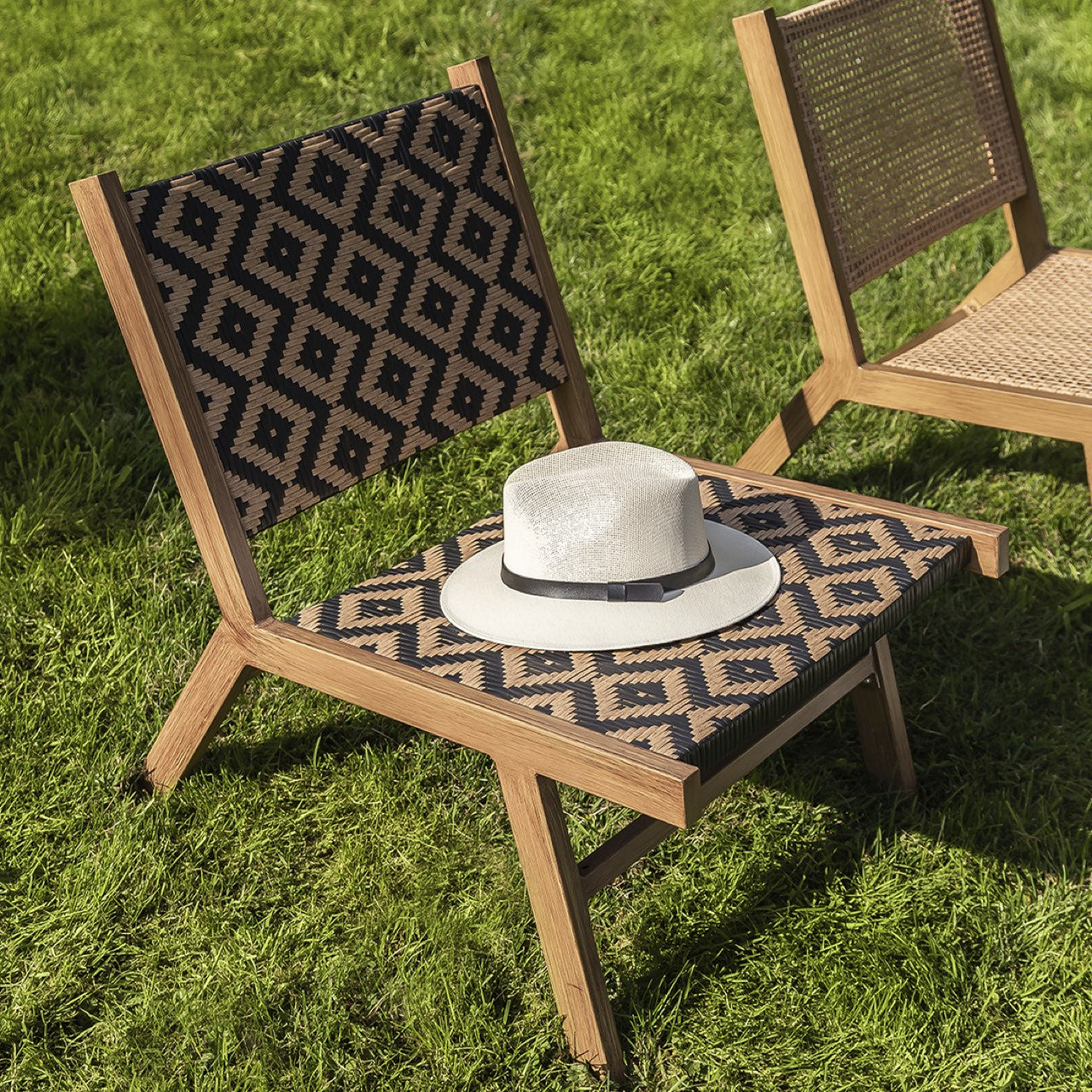 Wooden chair with patterned seat and backrest on grass, featuring a white hat.