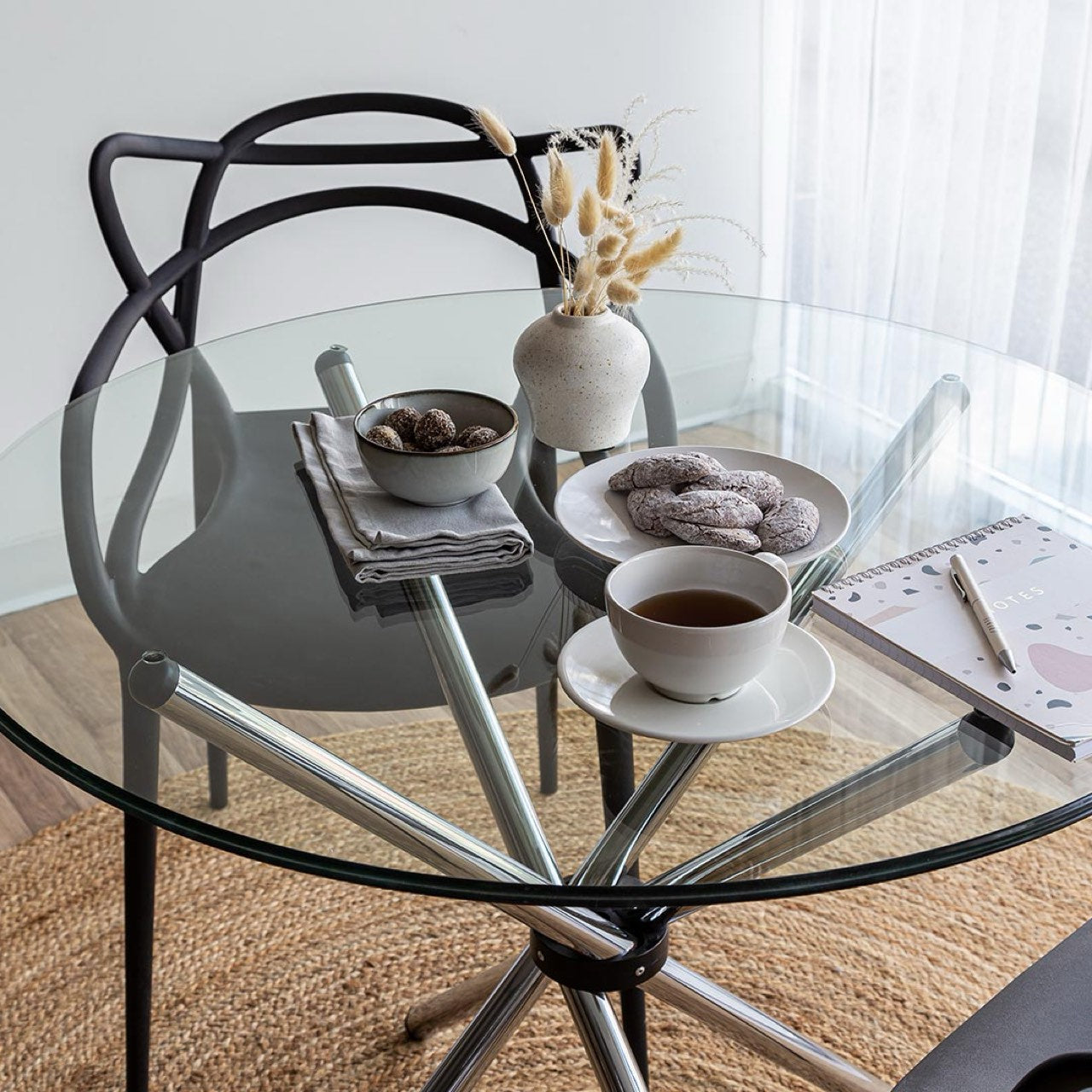 Round glass table with metal legs, chair, and a cup of coffee on a rug.