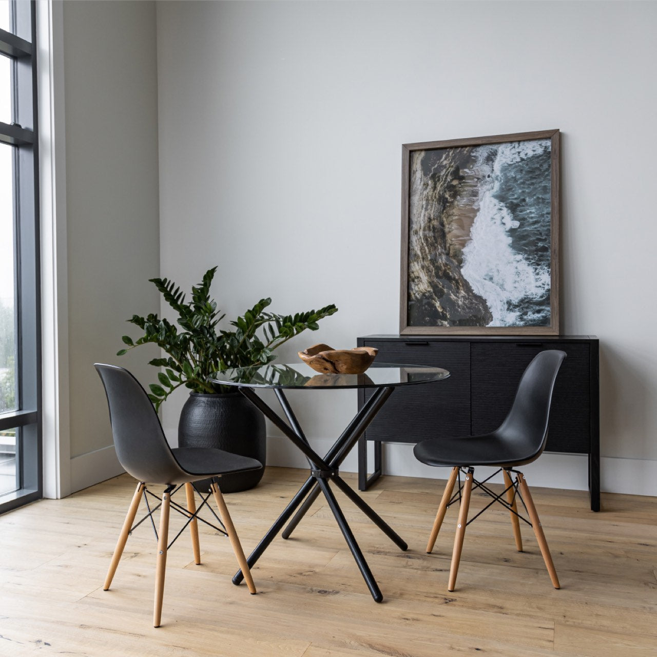 Modern dining area with black chairs, glass table, and framed artwork on a white wall.