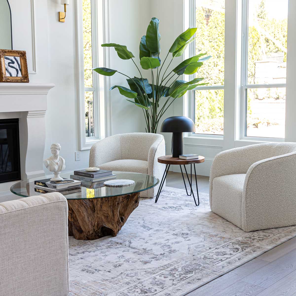 Modern living room with beige armchairs, a glass coffee table, and a large plant.