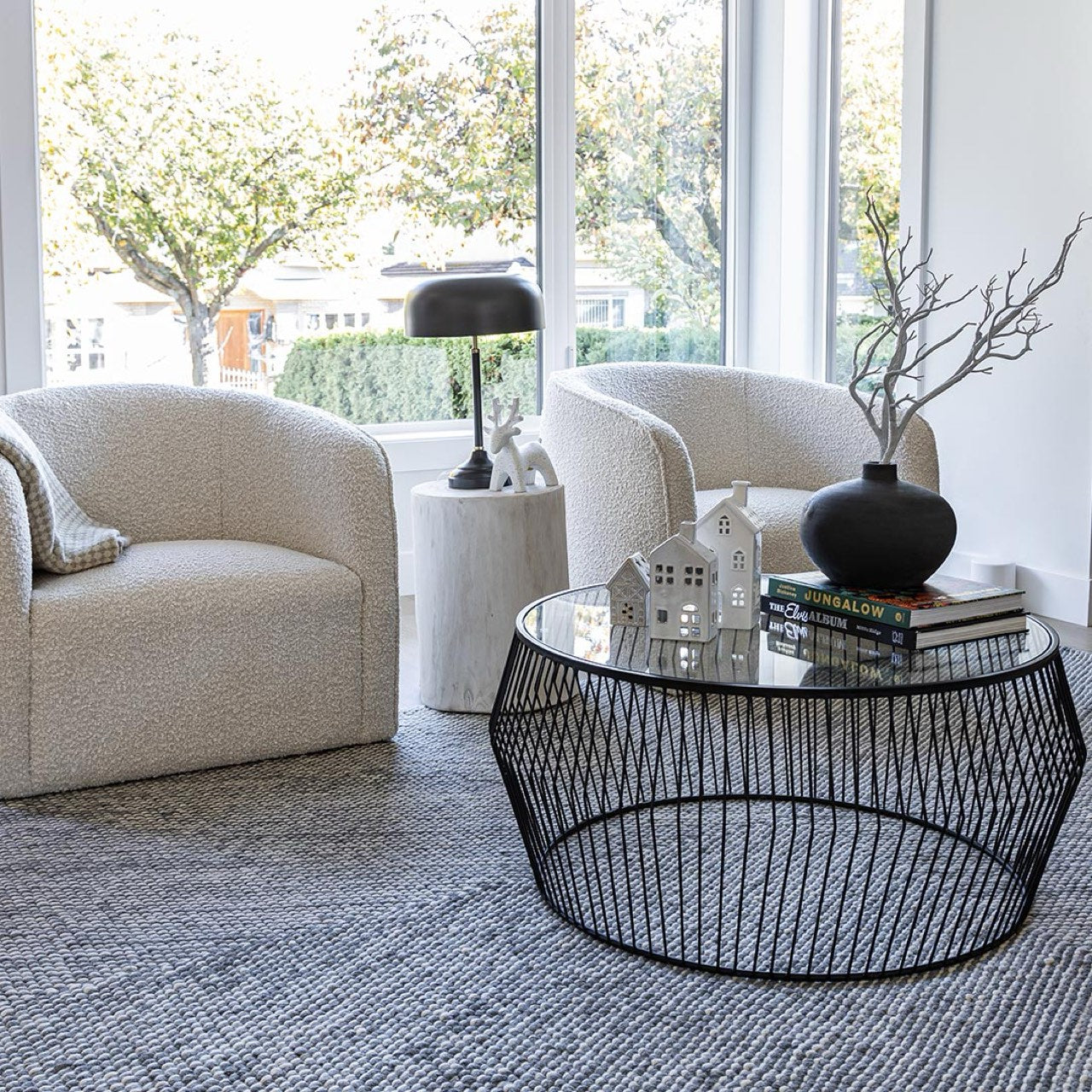 Modern living room with beige armchairs, a glass coffee table, and decorative items.