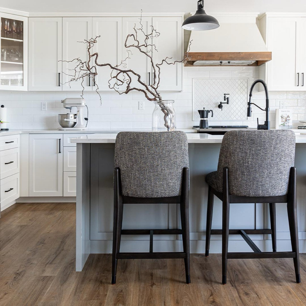 Modern kitchen with white cabinets, wooden floor, and gray bar stools.