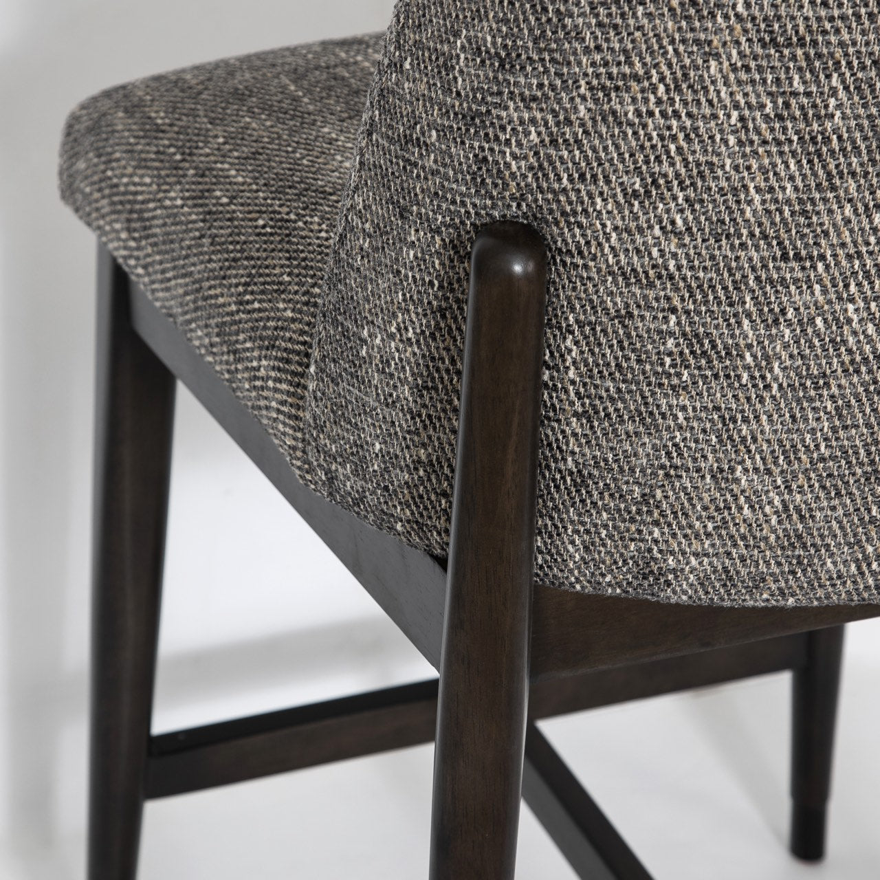 Close-up of a chair with dark wooden legs and gray textured fabric seat on a light background
