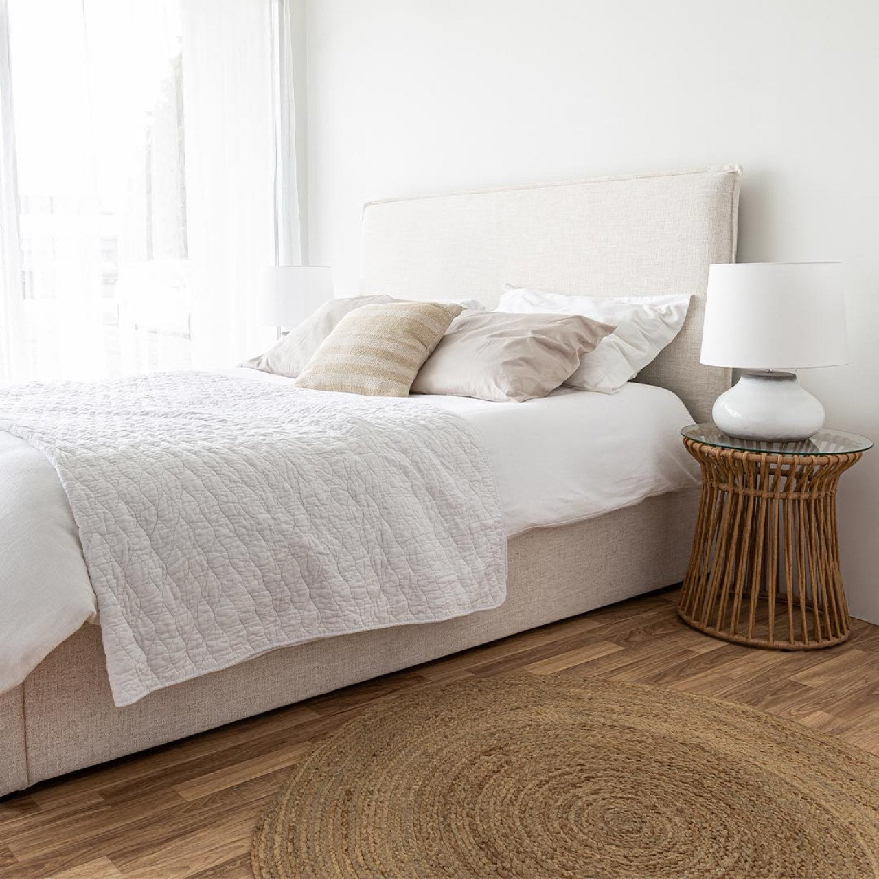 Neatly made bed with beige pillows and a lamp on a side table in a bedroom.