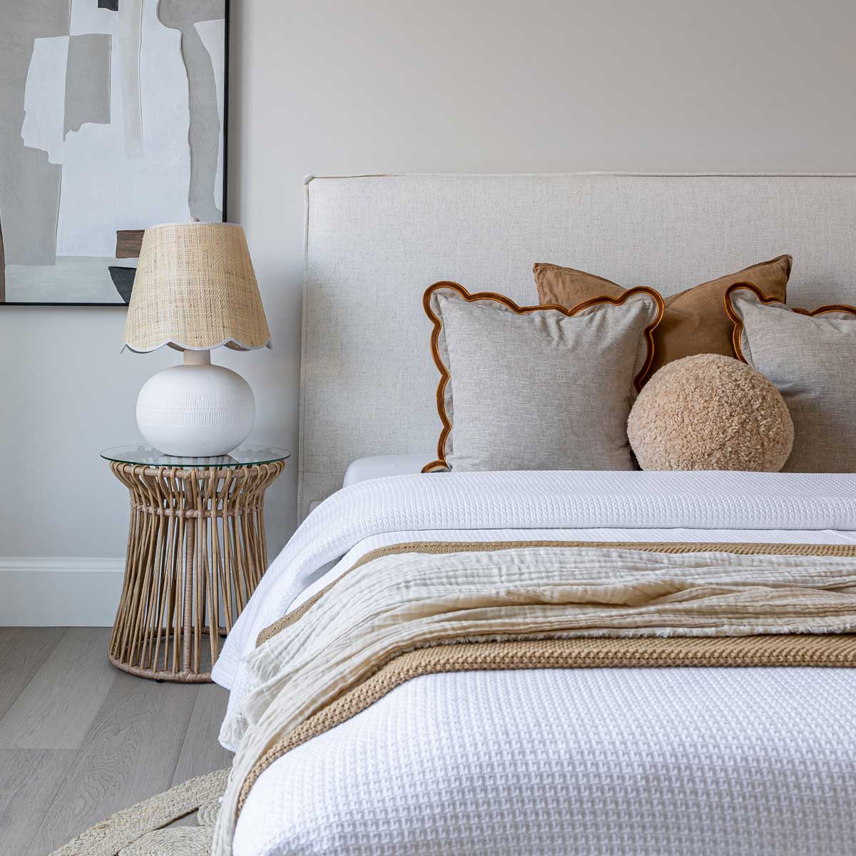 Neatly made bed with decorative pillows and a lamp on a side table in a bedroom.