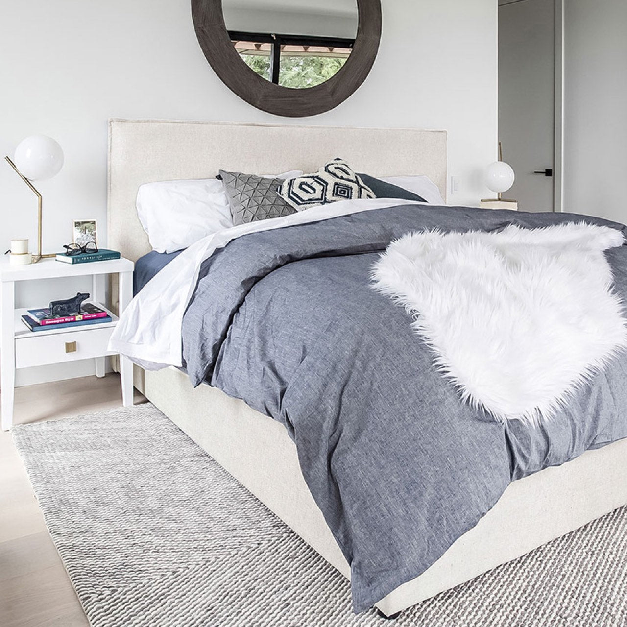 Modern bedroom with gray bedding and white fur throw on a bed.