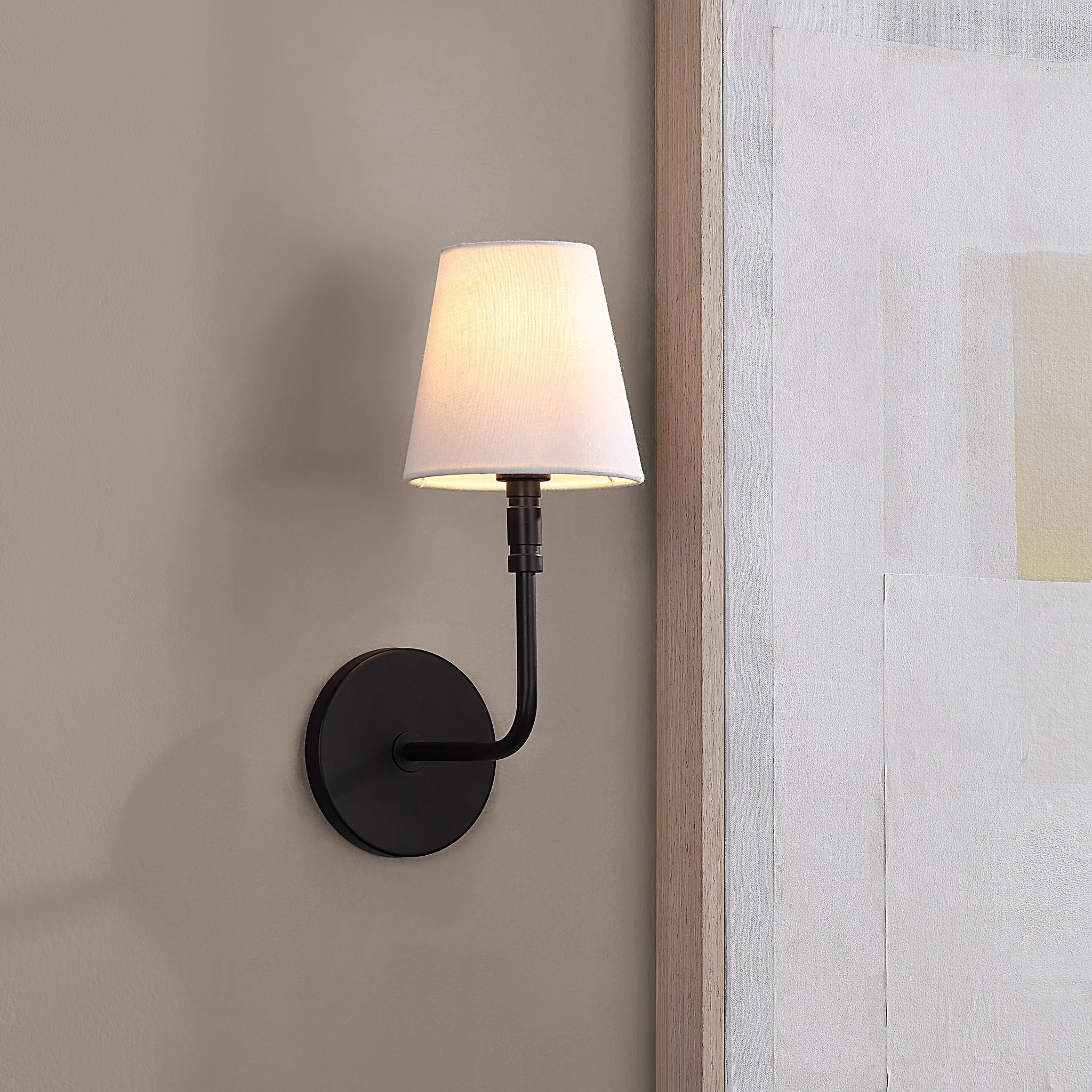 Andi Wall Sconce installed on a wall, illuminating a beige background with a soft glow.