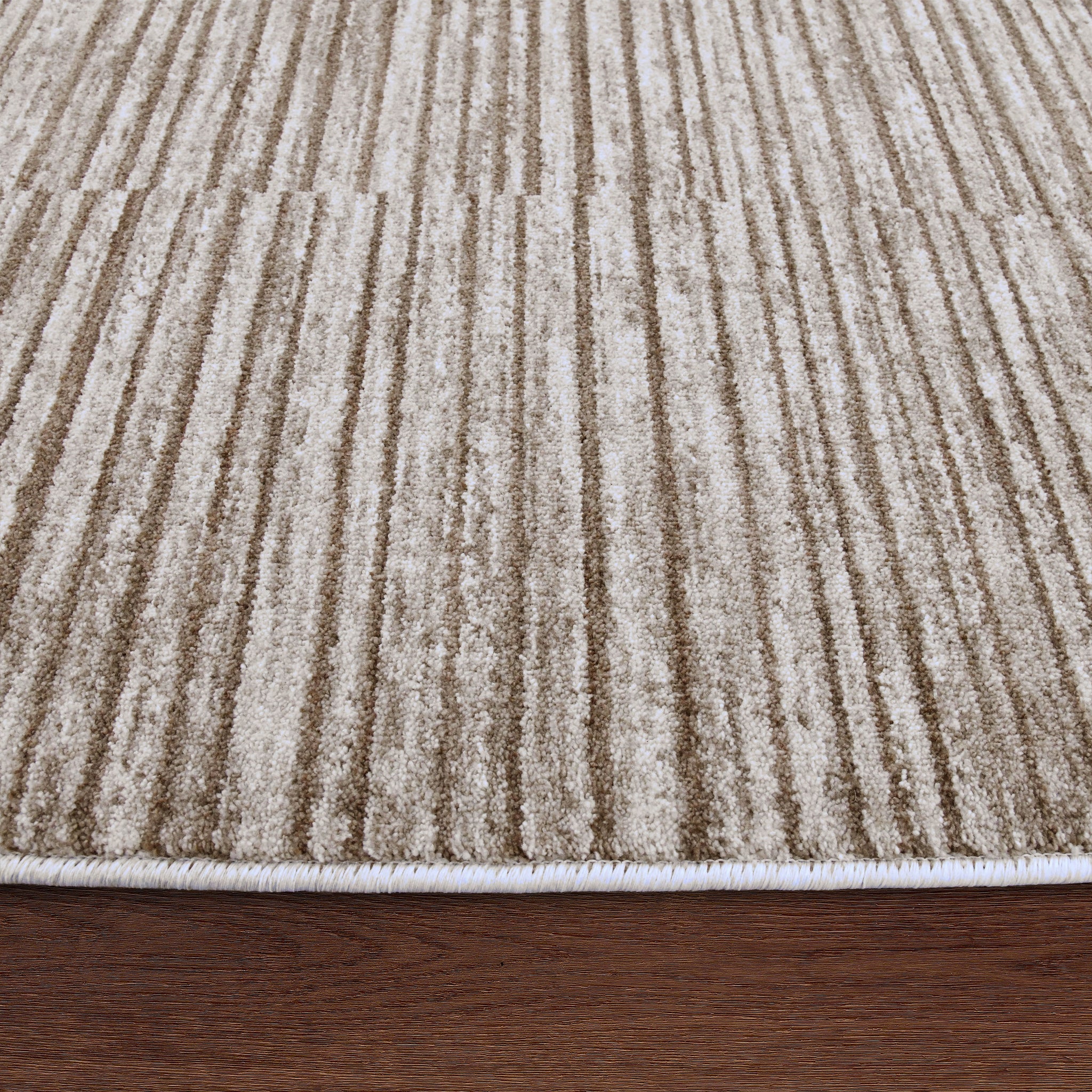 Blake rug featuring a textured striped pattern in beige and cream, with a white edge on a wooden surface.