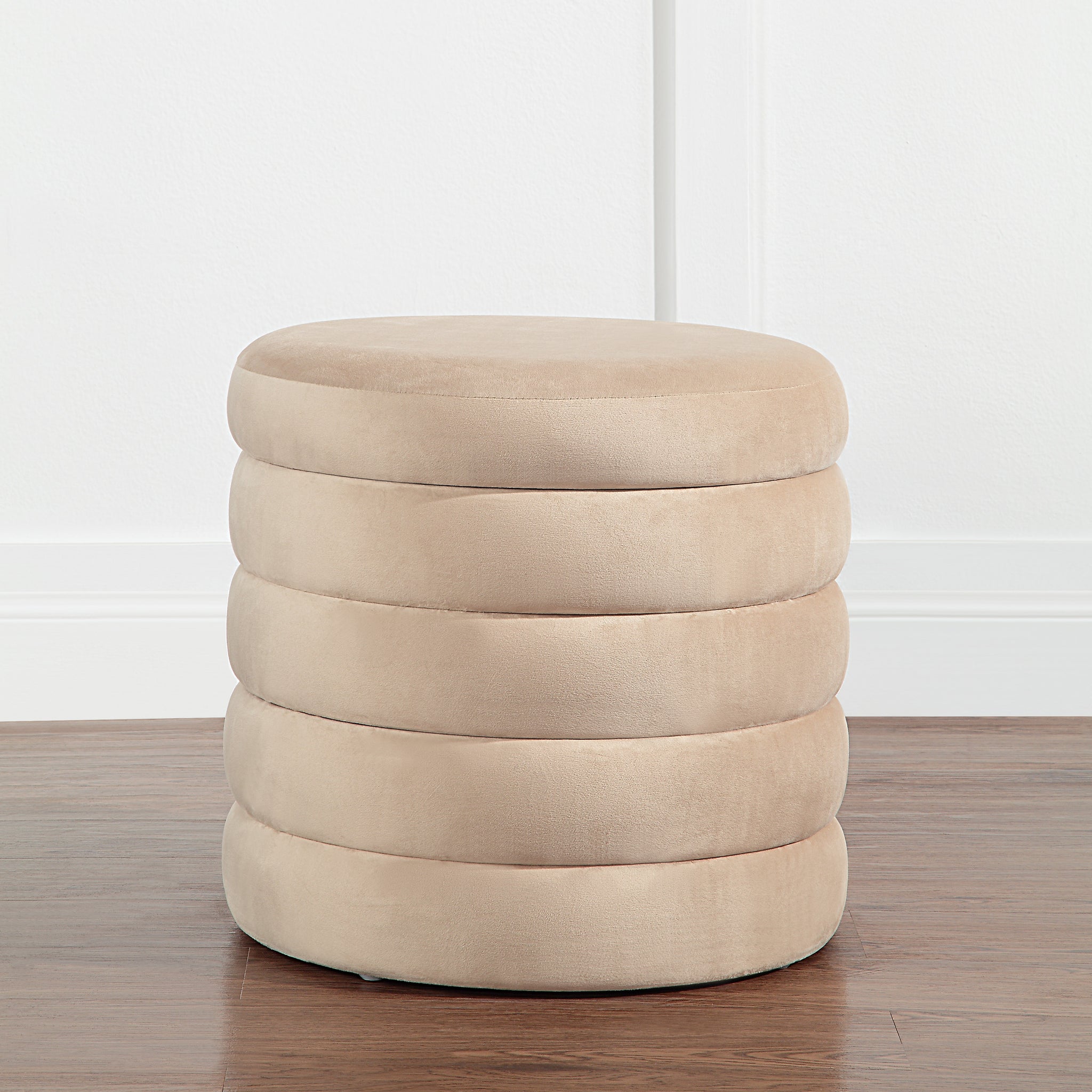Lloyd Storage Ottoman in beige, positioned on a wooden floor against a white wall.