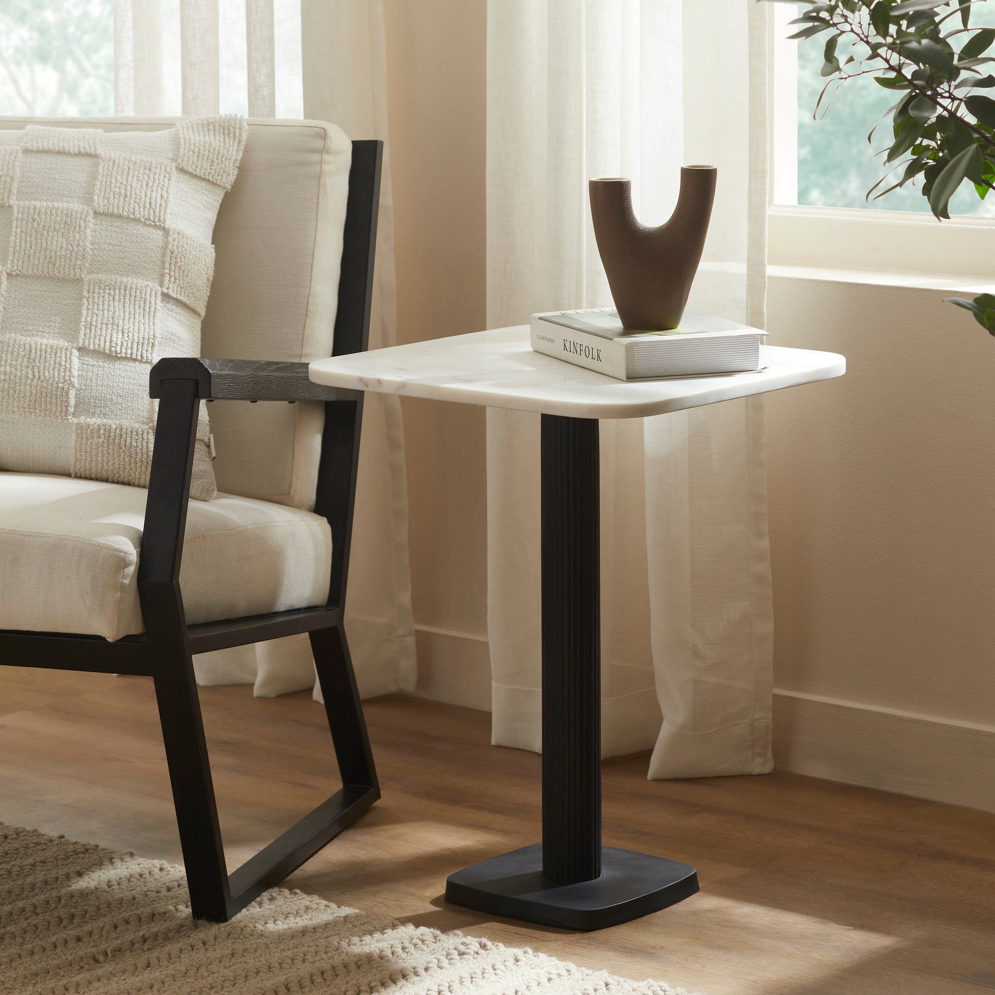 Laila Side Table beside a chair, styled with a vase and book on top.