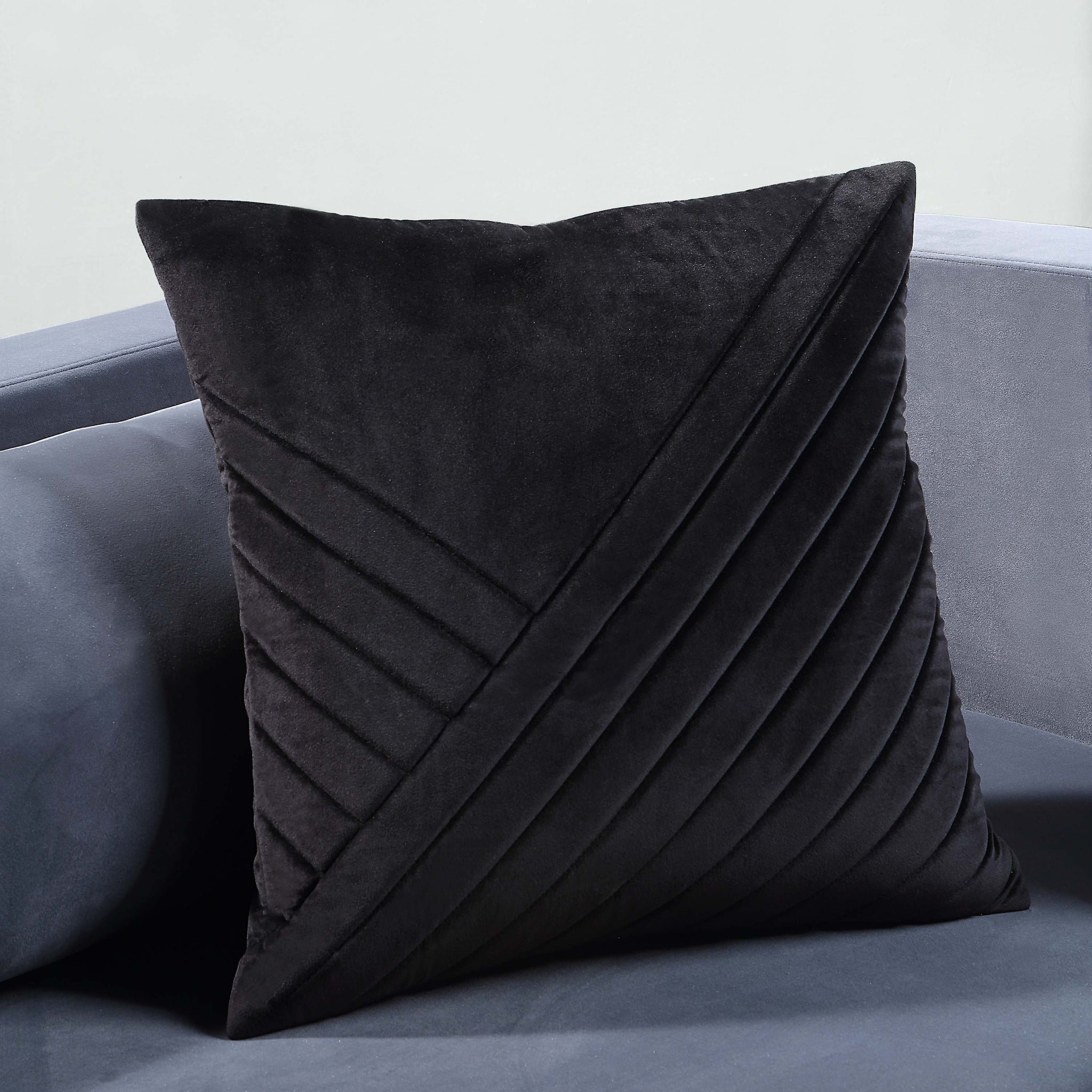 Diran Indoor Pillow in black placed on a gray sofa, featuring diagonal quilted design