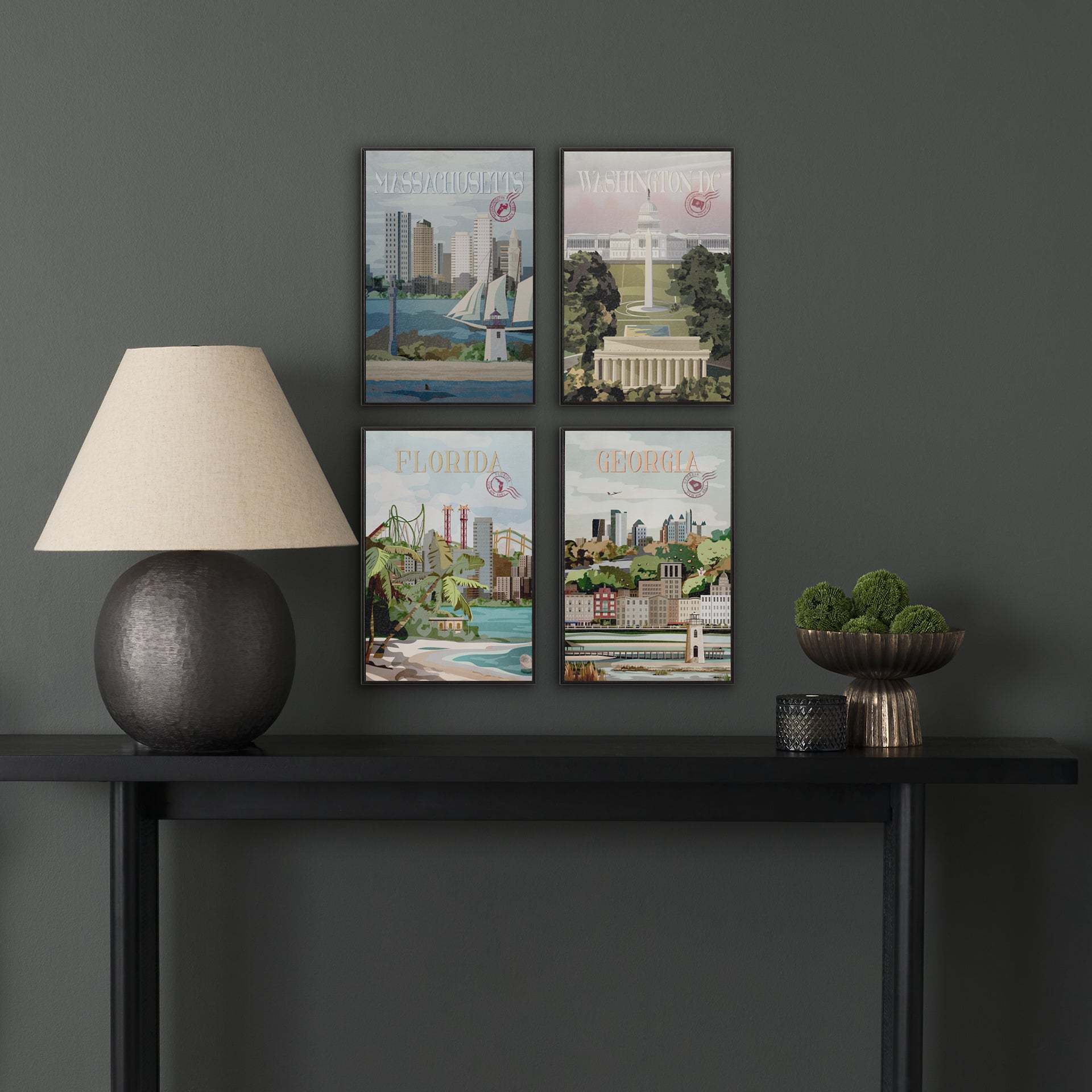 Four framed artworks on a dark wall above a black console table with decorative items.