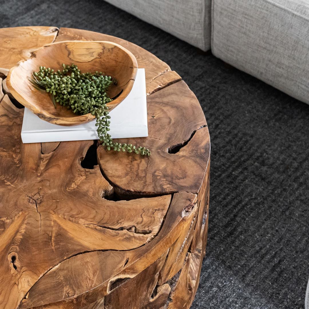 Wooden coffee table with a bowl of greenery on a dark carpeted floor.