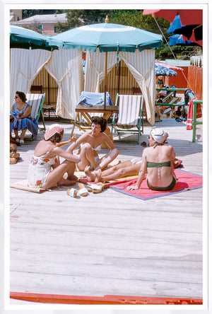 Toni Frissell – Gossip Riviera C. 1954, women relaxing on a beach with umbrellas and lounge chairs.