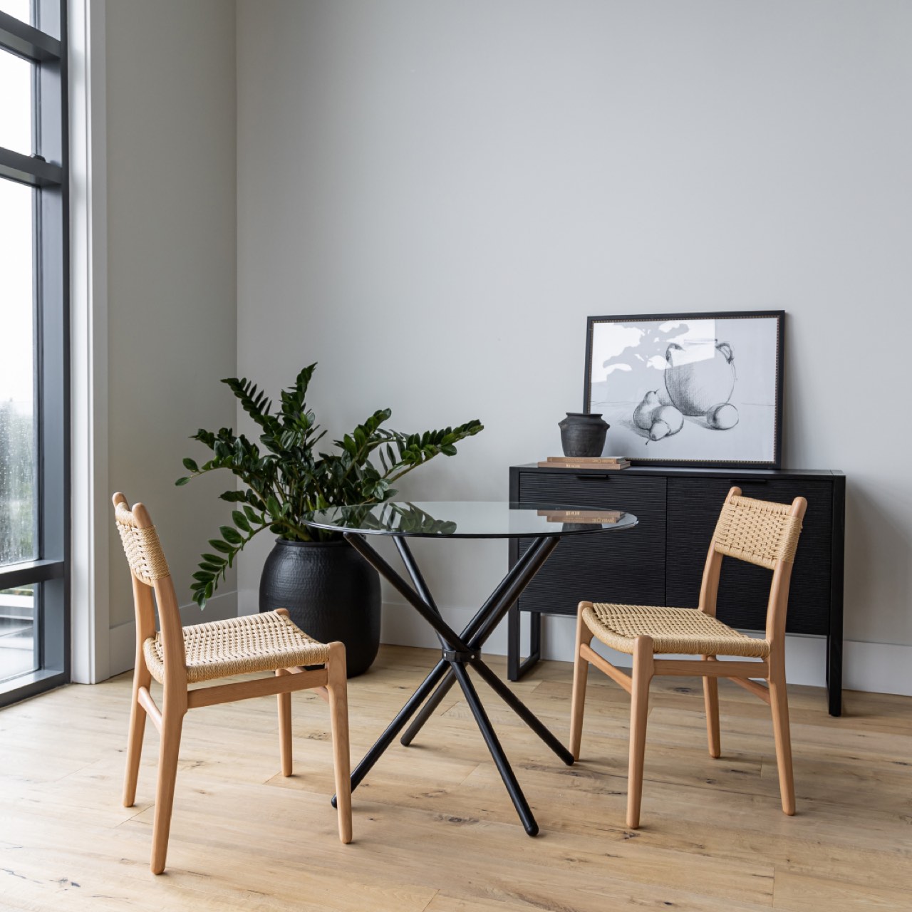 Modern dining area with glass table, wooden chairs, and a plant.