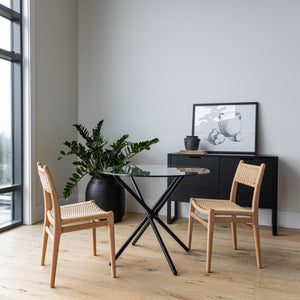 Modern dining area with glass table, wooden chairs, and a plant.
