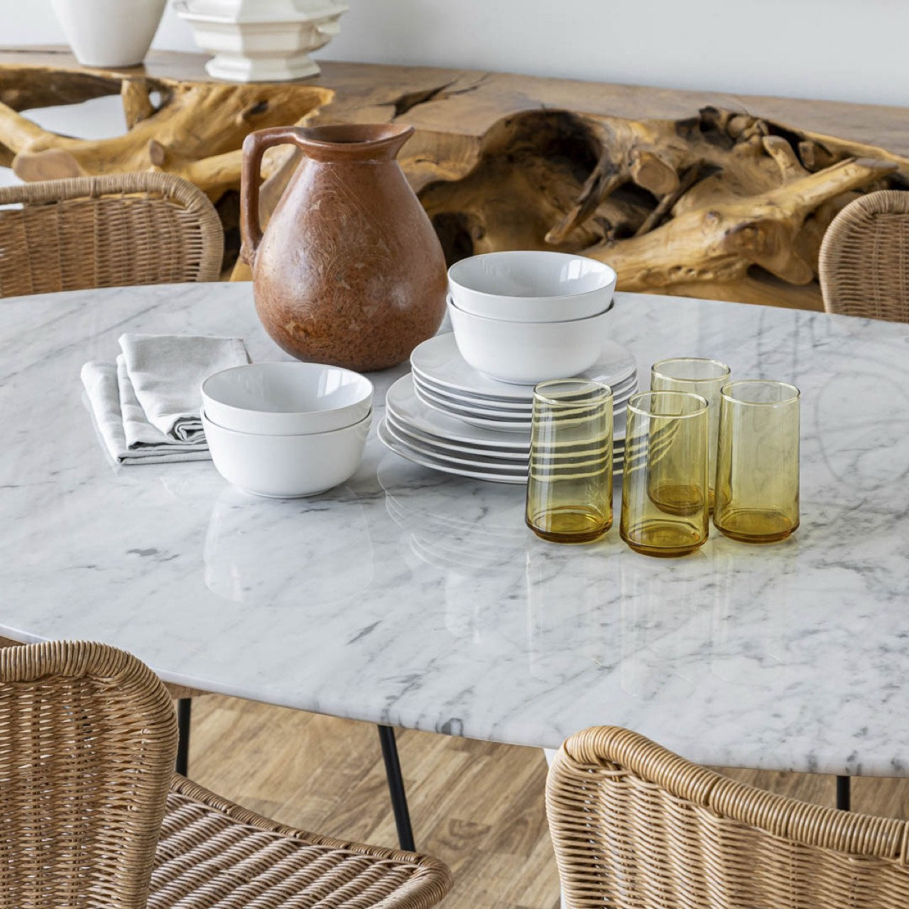Dining table with marble surface, ceramic bowls, a brown pitcher, and glassware on a wooden floor.