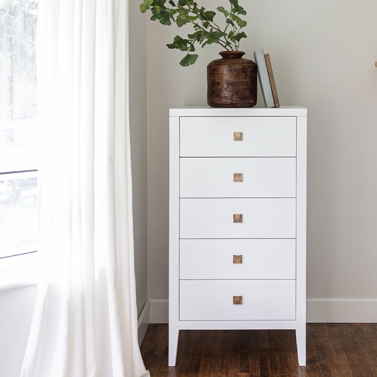 White dresser with four drawers and bronze handles on a white background
