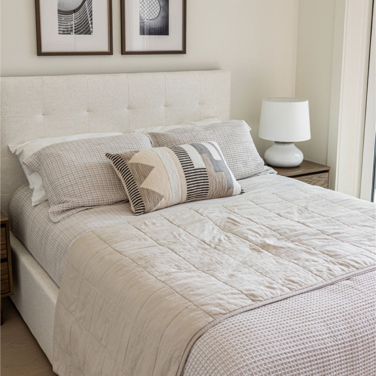 Neatly made bed with decorative pillows and a lamp in a bedroom setting.