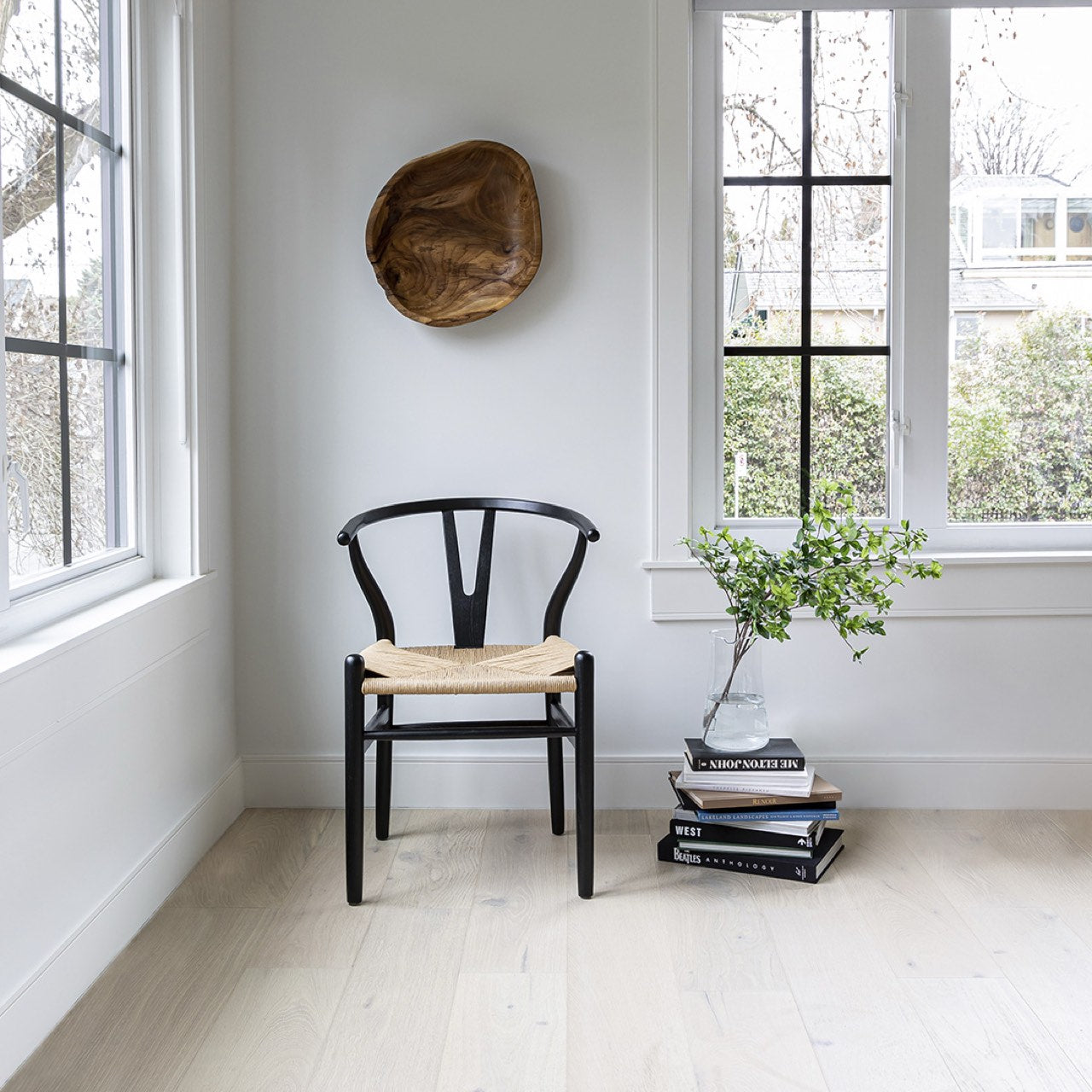 Black chair with a woven seat in a room with large windows and a wooden bowl on the wall.