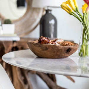 Wooden bowl with food on a marble table next to a vase of flowers