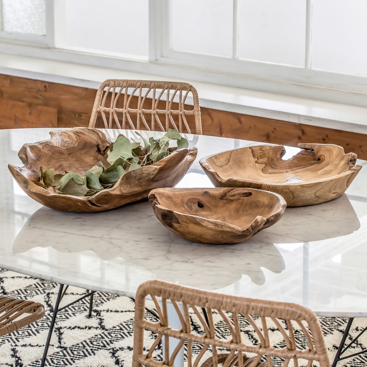 Three wooden bowls on a marble table with wicker chairs in a bright room.