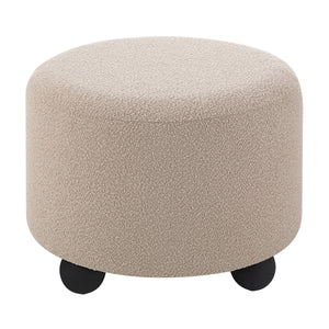 Claude Ottoman featuring a soft beige texture and rounded design with black feet