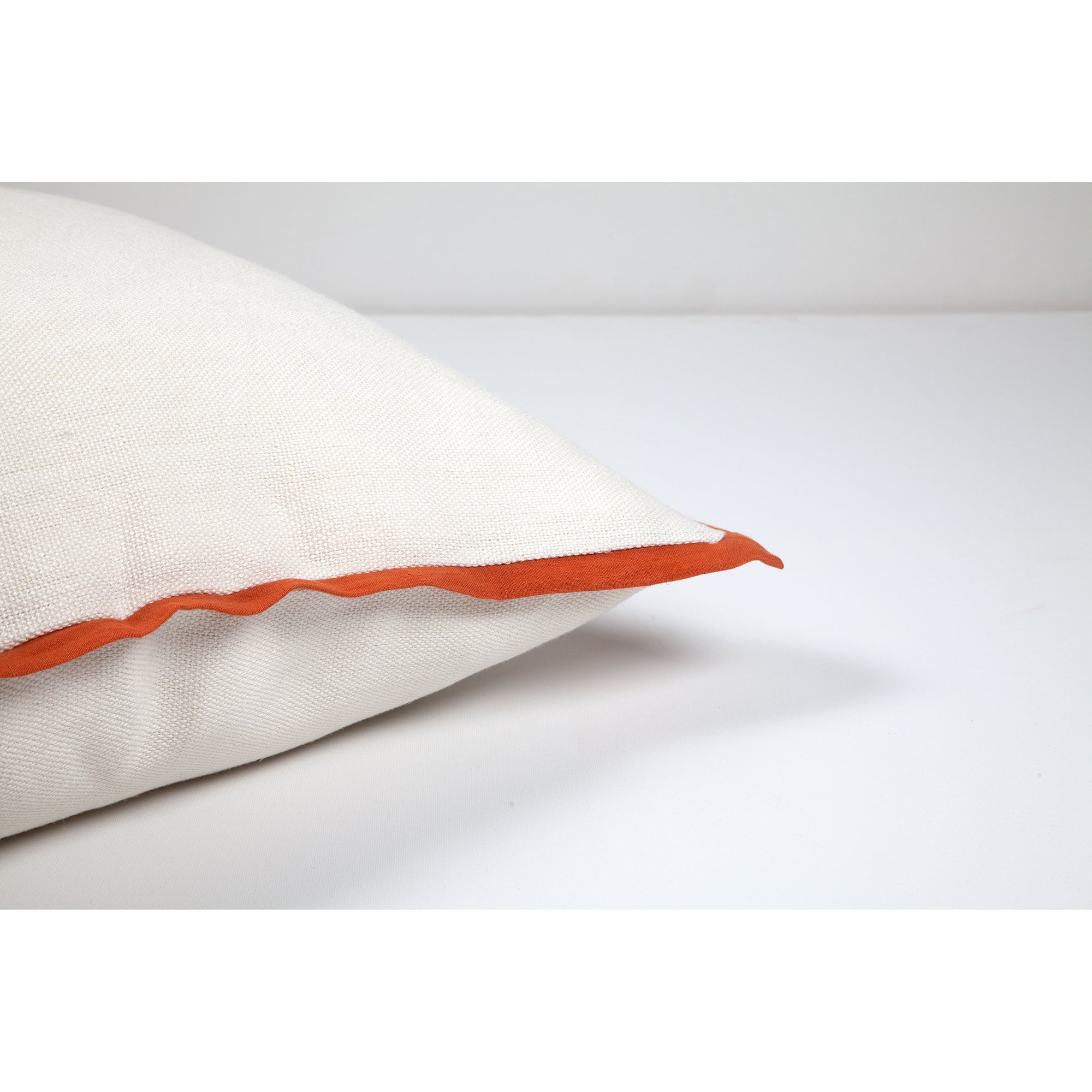 Elise Indoor Pillow featuring white fabric and orange piping, angled view