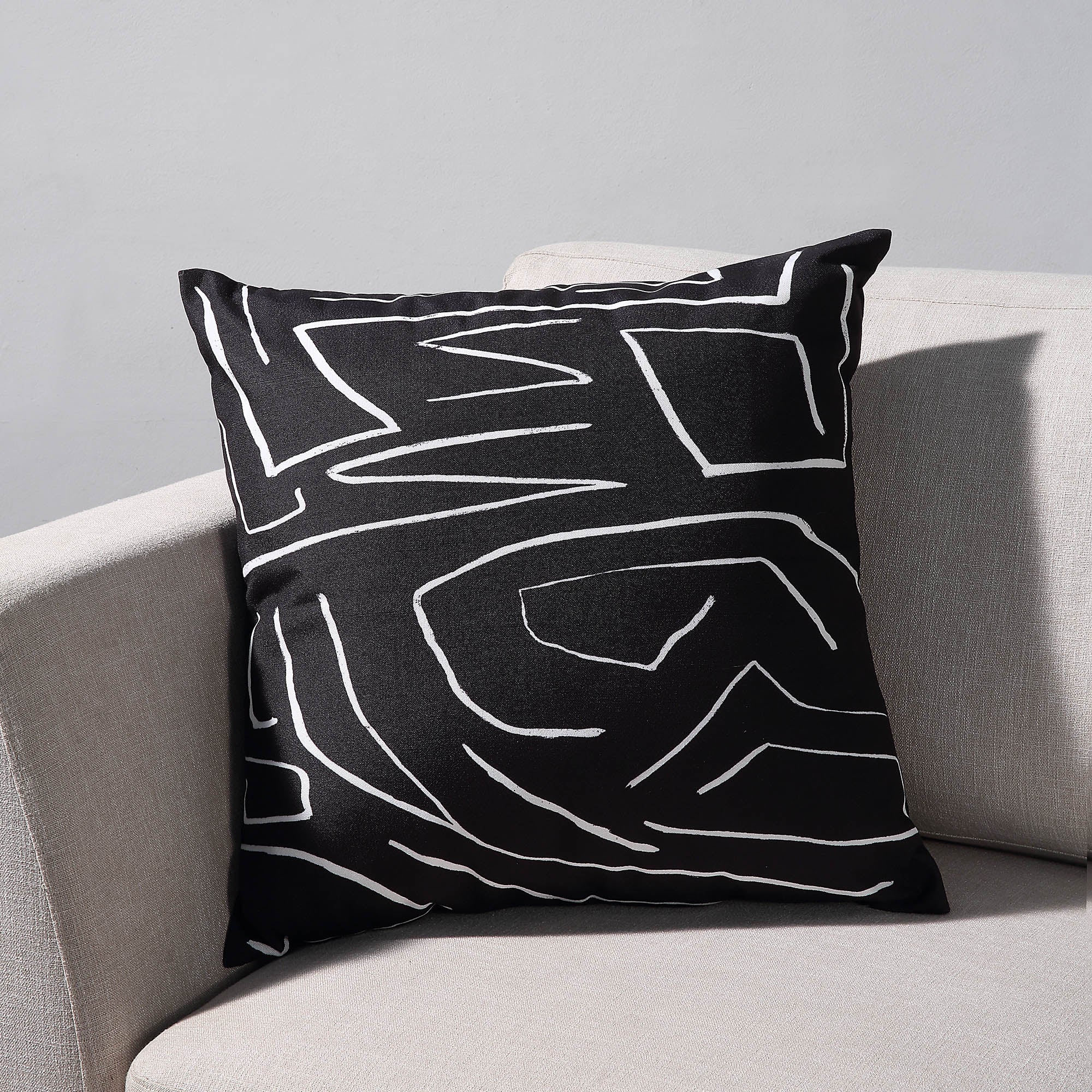 Ray Indoor Pillow on a light sofa, featuring a black fabric with white abstract lines.