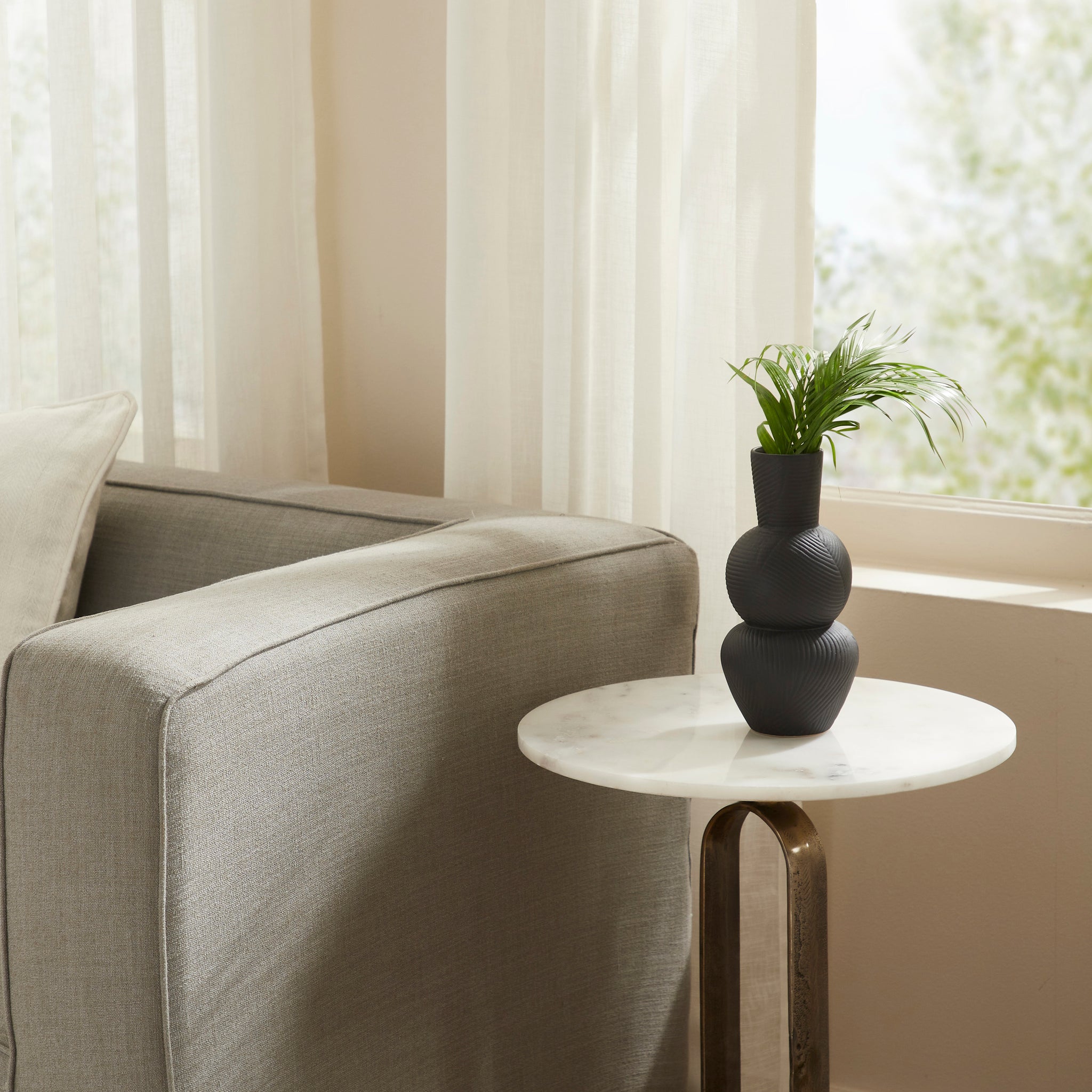 Icarus Vase placed on a marble table beside a sofa, adorned with faux greenery.