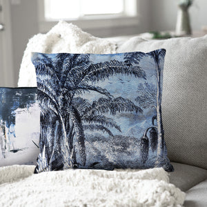 Jona Indoor Pillow with a blue palm tree print, placed on a cozy couch with a throw blanket.