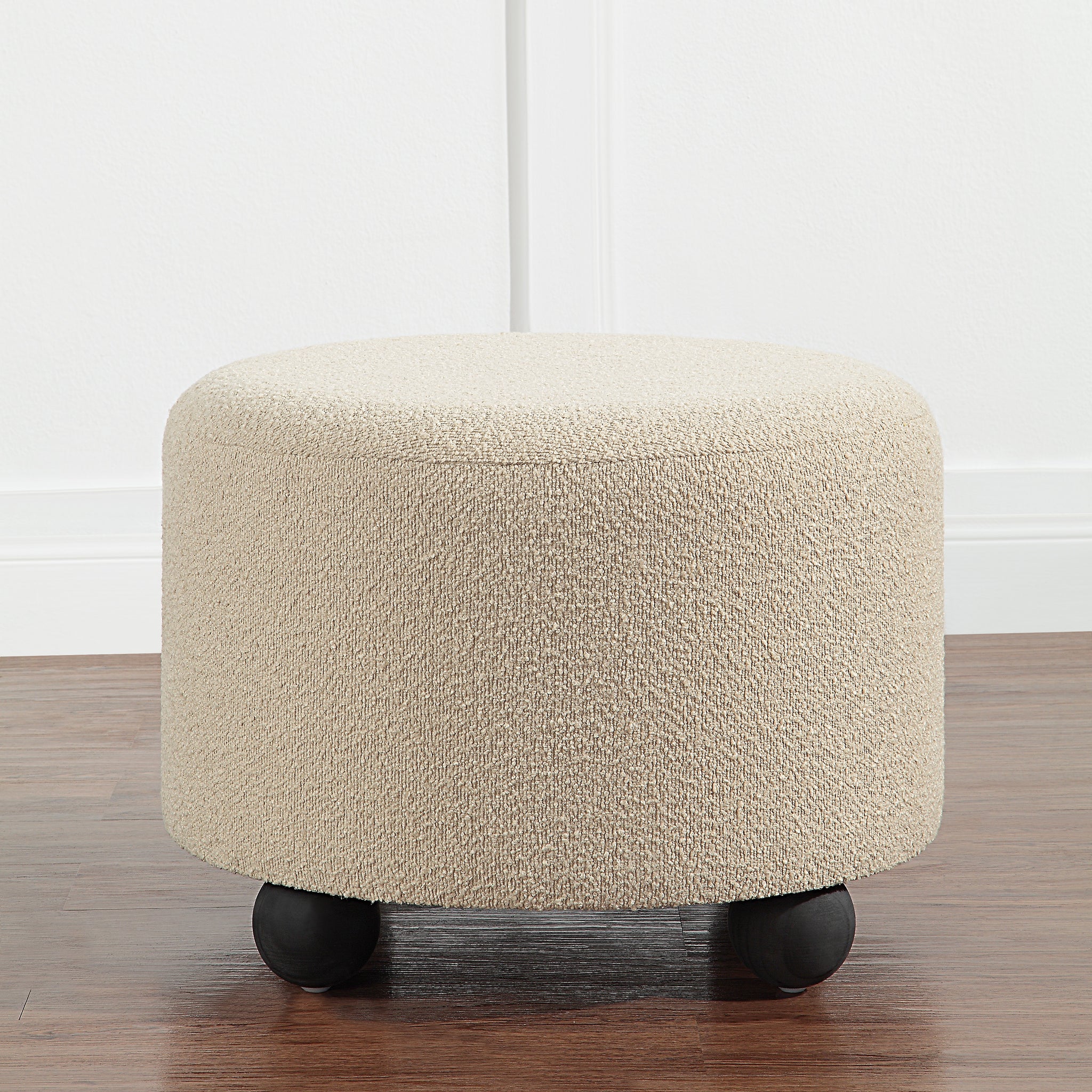 Claude Ottoman in beige, round shape, set against a white wall background