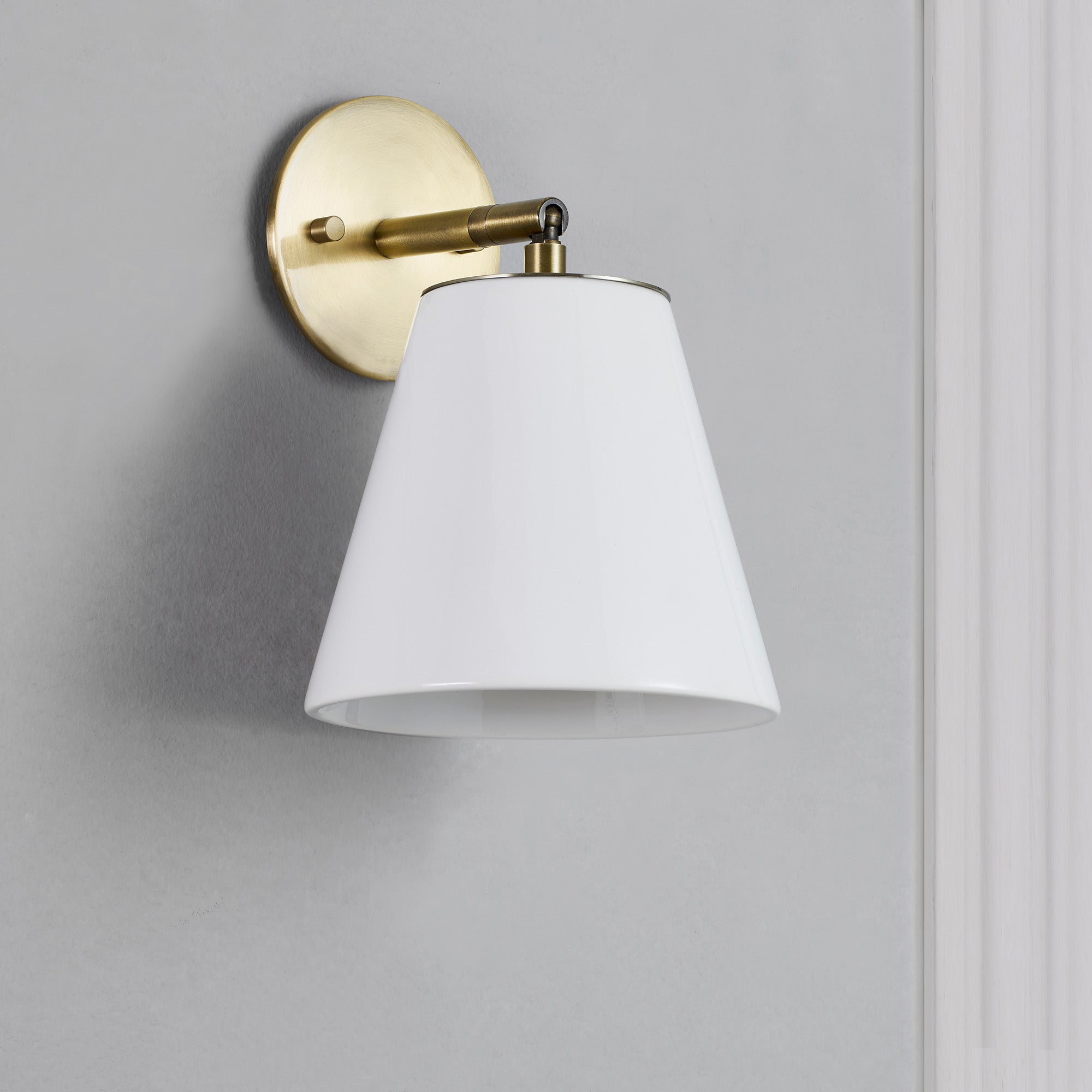 Kai Wall Sconce mounted on a gray wall, showcasing white shade and brass details.