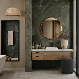 Canna mirror with a round wooden frame above a modern bathroom vanity, featuring green stone tiles and decorative vases.