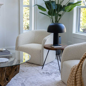 Modern living room with beige armchair, glass coffee table, and black lamp.
