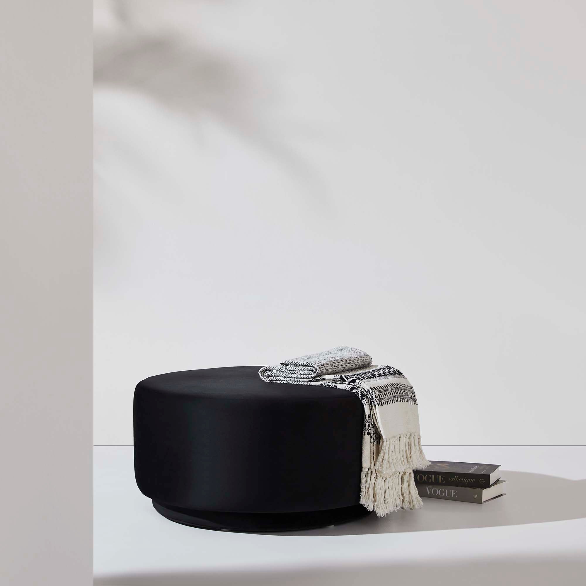 Colum Ottoman in black, styled with a blanket and books, minimalist background.