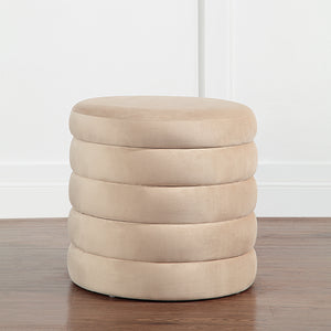 Lloyd Storage Ottoman in beige, positioned on a wooden floor against a white wall.