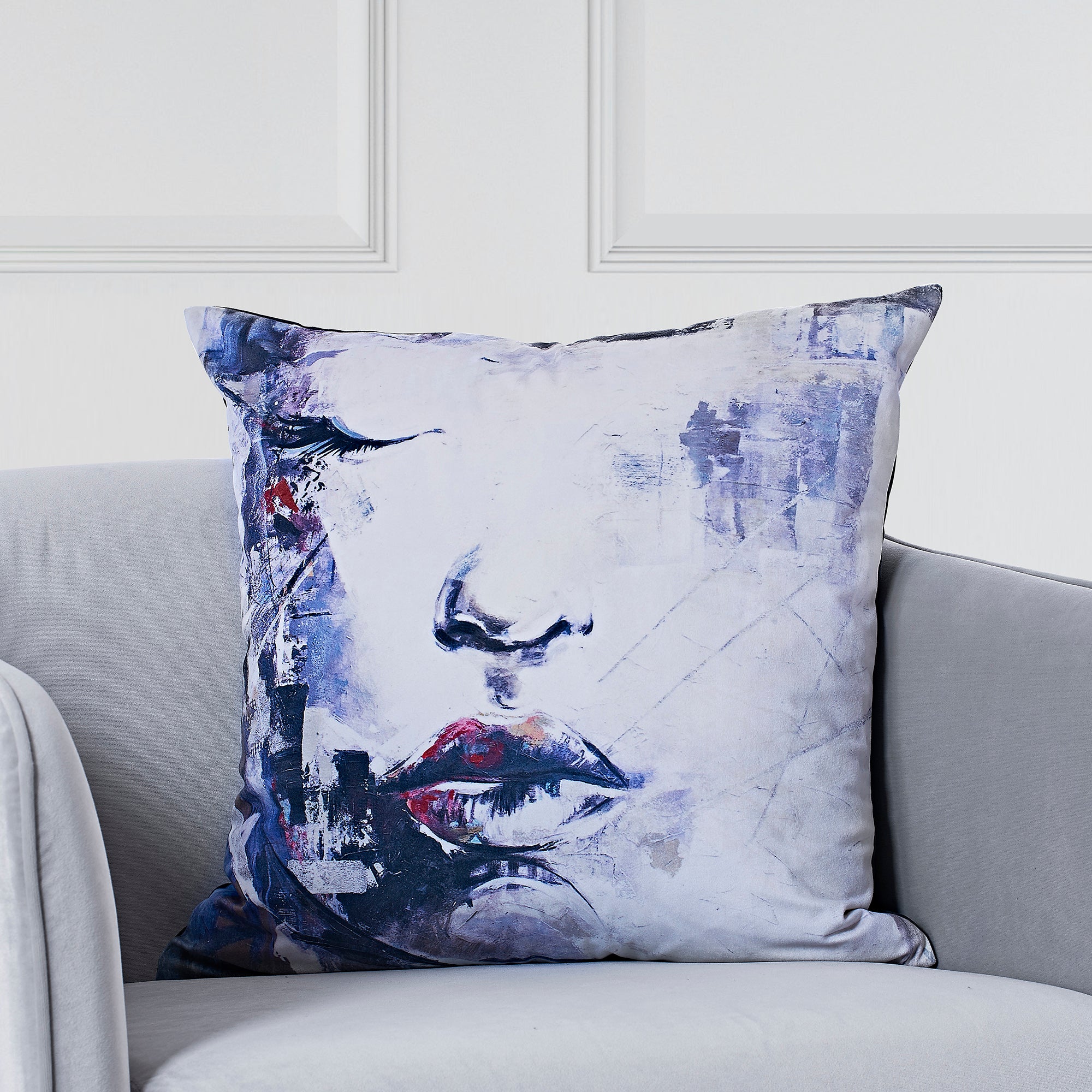 Annika Indoor Pillow displayed on a gray sofa, showcasing abstract face design in blue and red