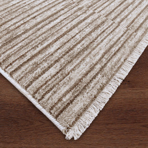 Corner view of Blake rug by Renwil in beige with fringed edges on a wooden floor.