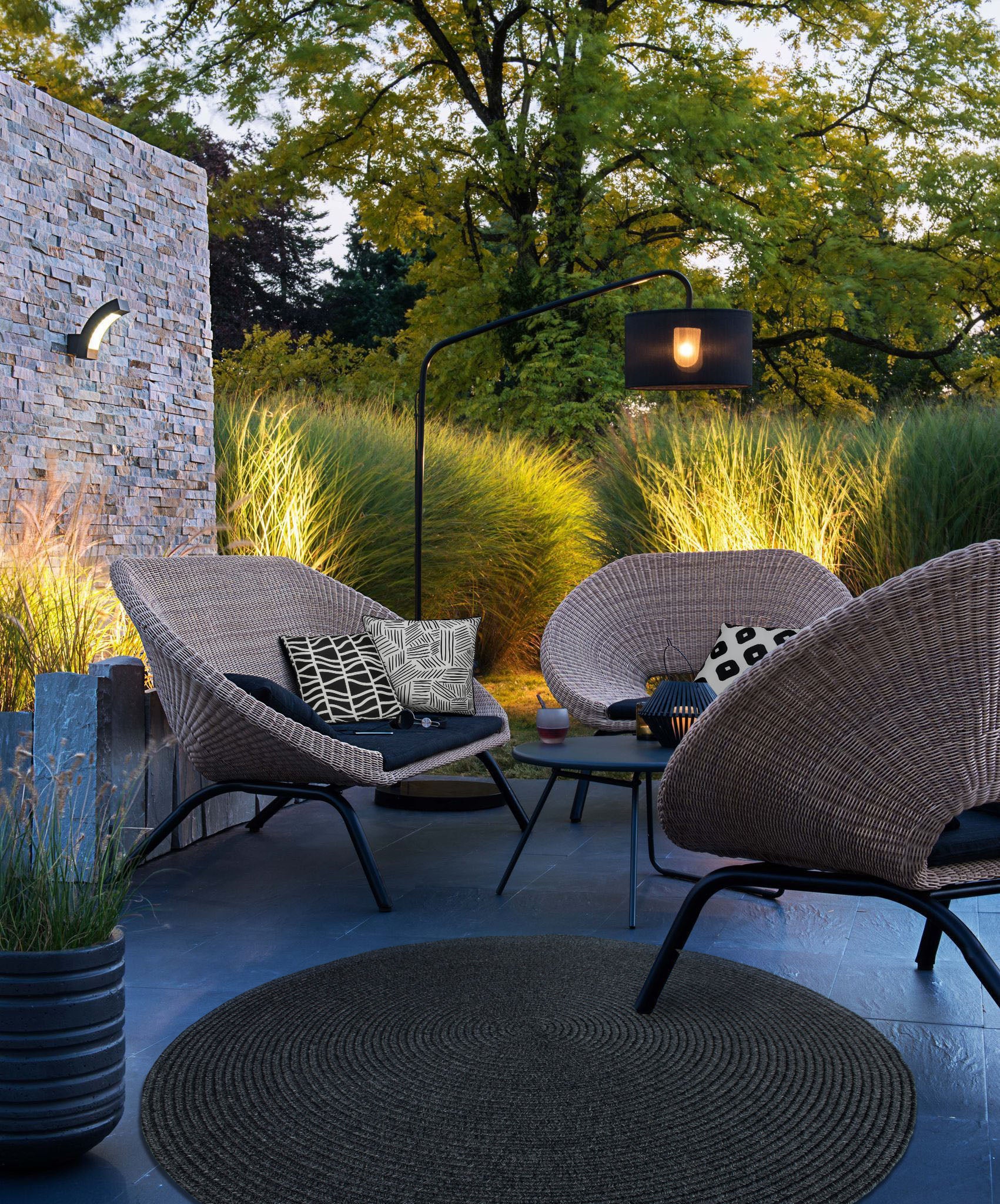 Outdoor seating area featuring Fieldfare Outdoor Pillows on wicker chairs, surrounded by greenery.