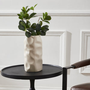 Hermione Vase by Renwil on a black table, filled with green foliage against a white wall.