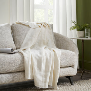 Ragusa Throw in white draped over a cozy sofa, styled with decorative pillows and a plant.