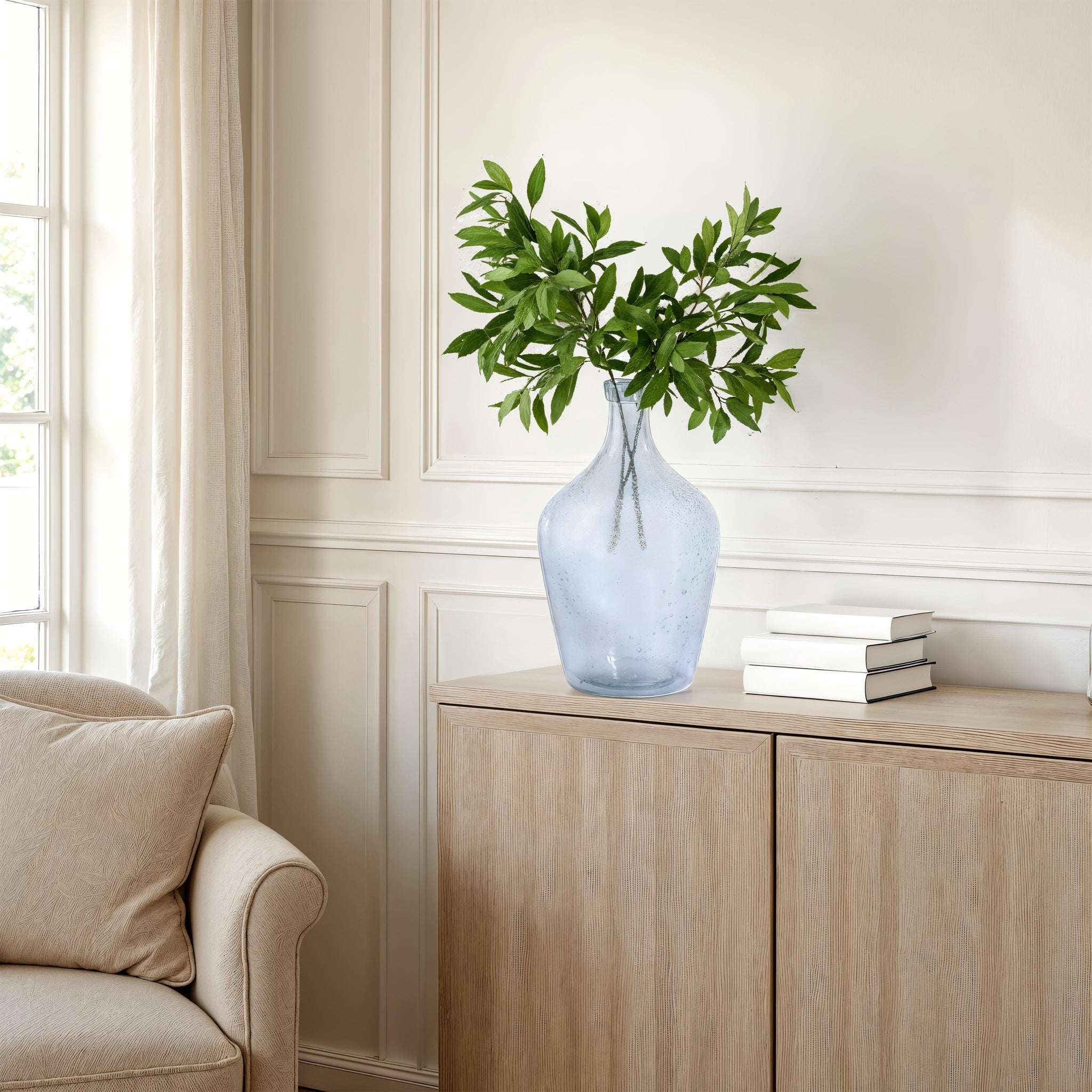 Mirabella vase by Renwil in light blue glass with green leaves, placed on a wooden cabinet.
