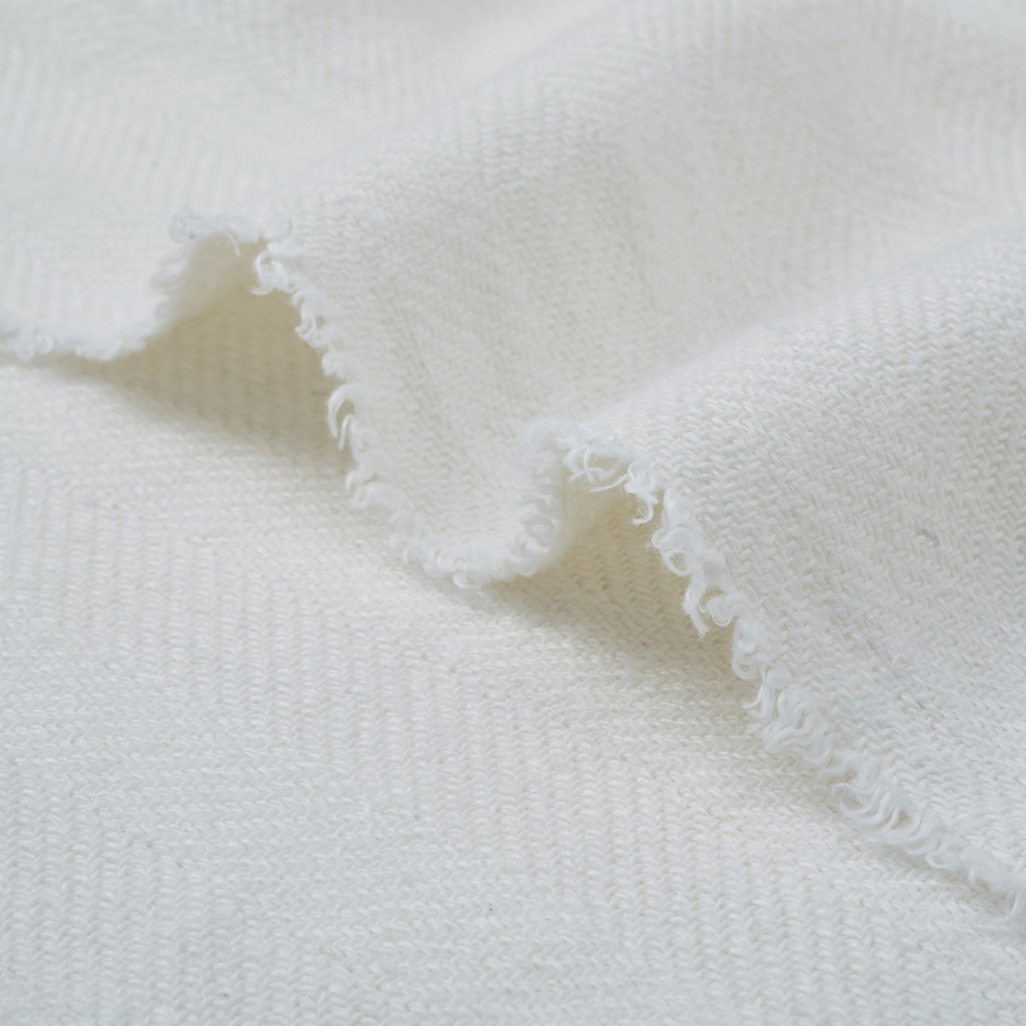 Ragusa Throw in white, highlighting the textured fabric with fringed edges laid flat.
