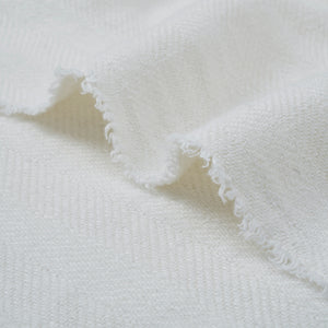 Ragusa Throw in white, highlighting the textured fabric with fringed edges laid flat.