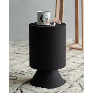 Oloria Stool in black with a coffee mug and sunglasses on top, placed on a patterned rug.